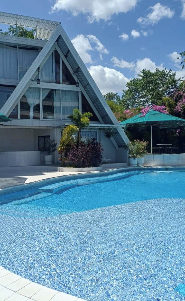 Un edificio moderno con piscina, rodeado de vegetación y un cielo despejado.