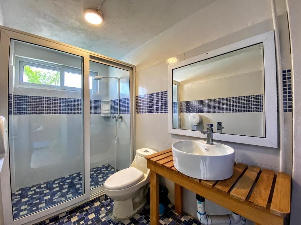 Une salle de bain avec une douche à parois de verre, des toilettes, un lavabo avec un miroir au-dessus et un sol carrelé.