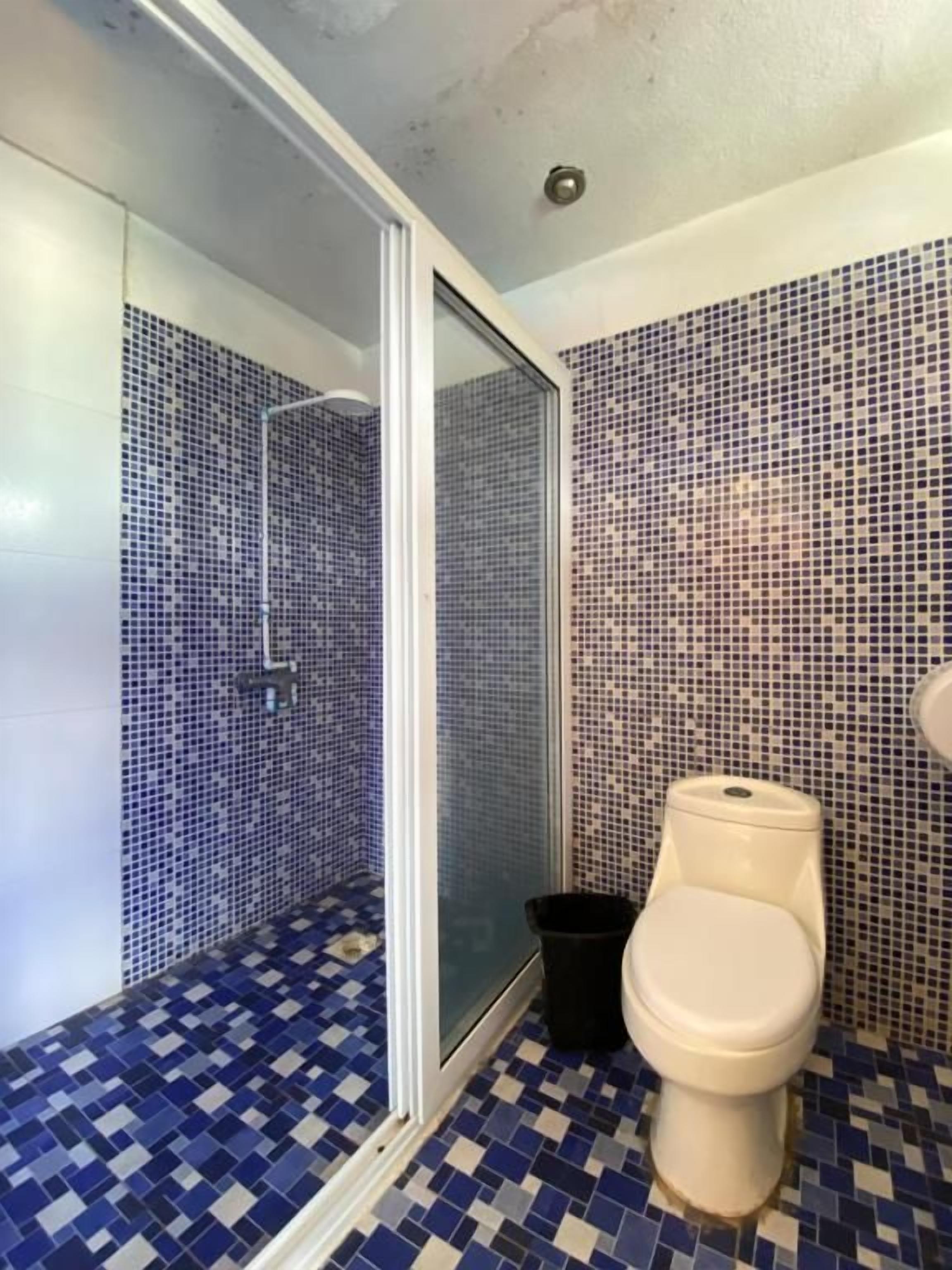 Un baño con ducha, inodoro y suelo de baldosas.