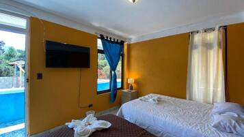 A hotel room with a bed, a TV mounted on the wall, a window with curtains, and a bedside table with a lamp.