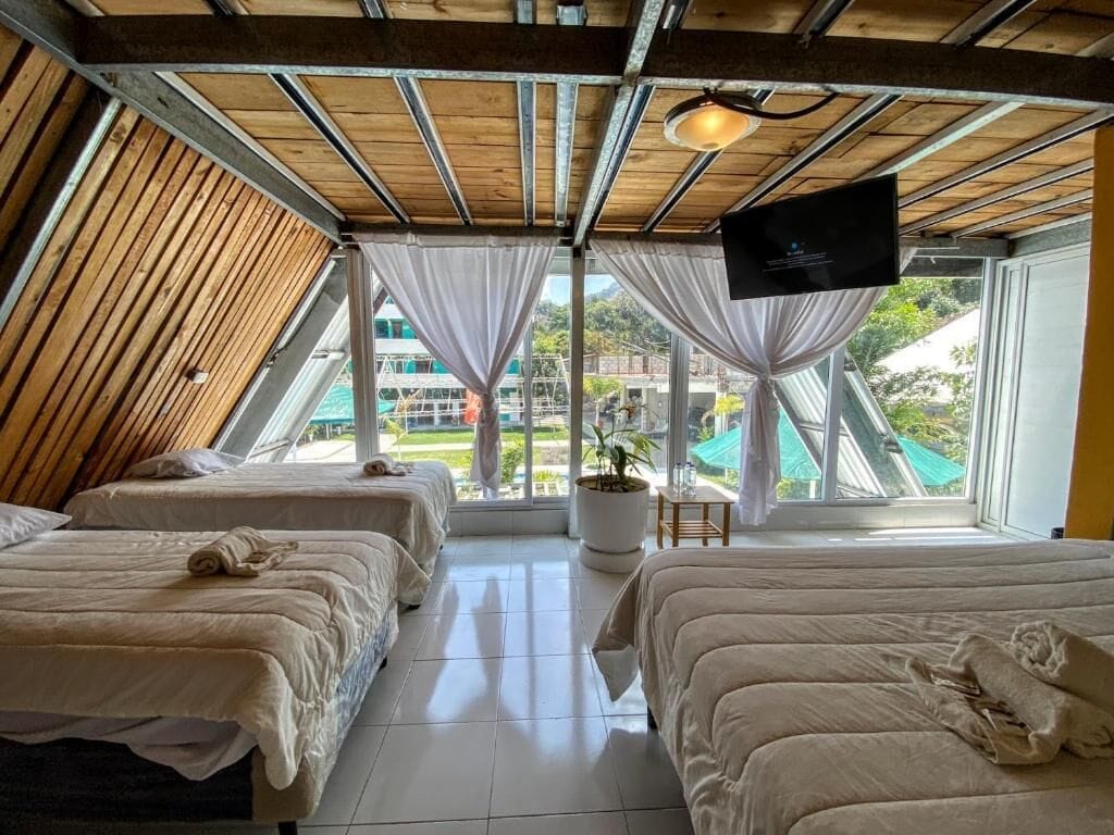 Una habitación con dos camas, un televisor montado en la pared y un ventanal con vistas al exterior.