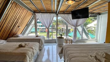 A room with two beds, a TV mounted on the wall, and a large window offering a view of the outdoors.