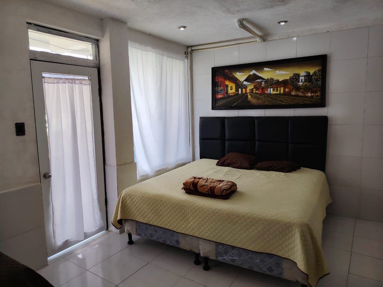 Une chambre à coucher avec un lit, des rideaux, un tableau et une porte.