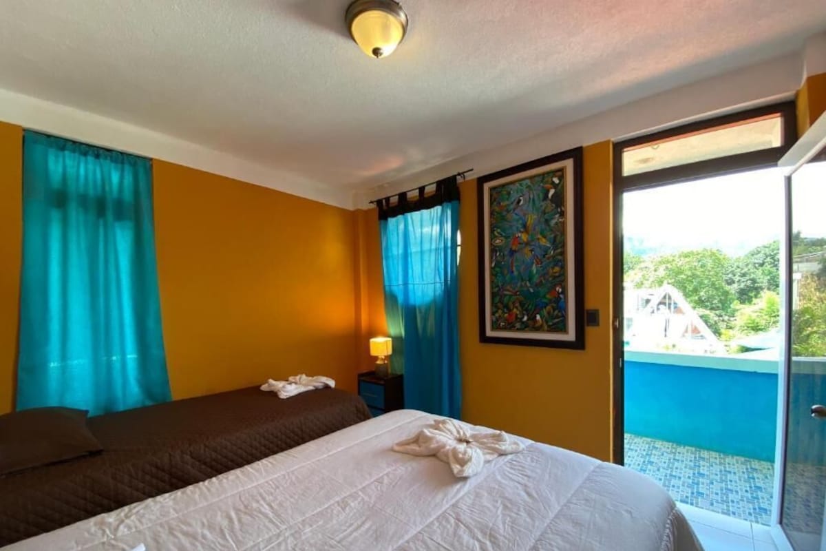 Una camera d'albergo con un letto, un comodino, una finestra con tende e vista sul verde.