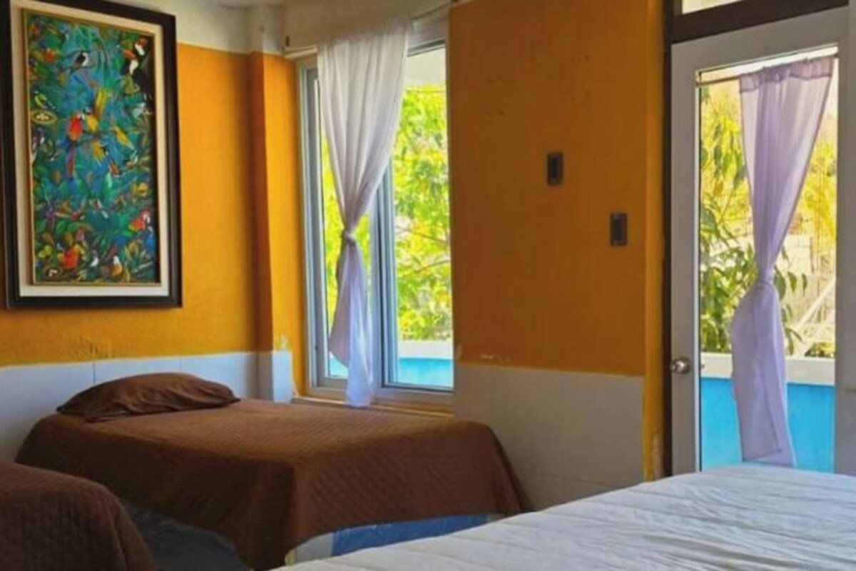 Una camera d'albergo con due letti, una finestra con tende, un quadro appeso al muro e vista su un edificio.