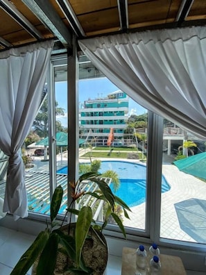 A room with a large window overlooking a swimming pool and a building.