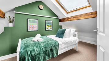 A bedroom with a sloped ceiling, a skylight, a bed with white bedding, a green wall, and two framed posters.