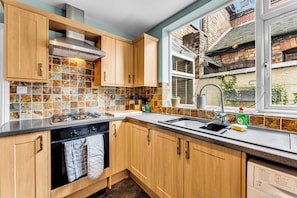 A kitchen with wooden cabinets, a tiled backsplash, a stainless steel range hood, and a window with a view of a brick building.