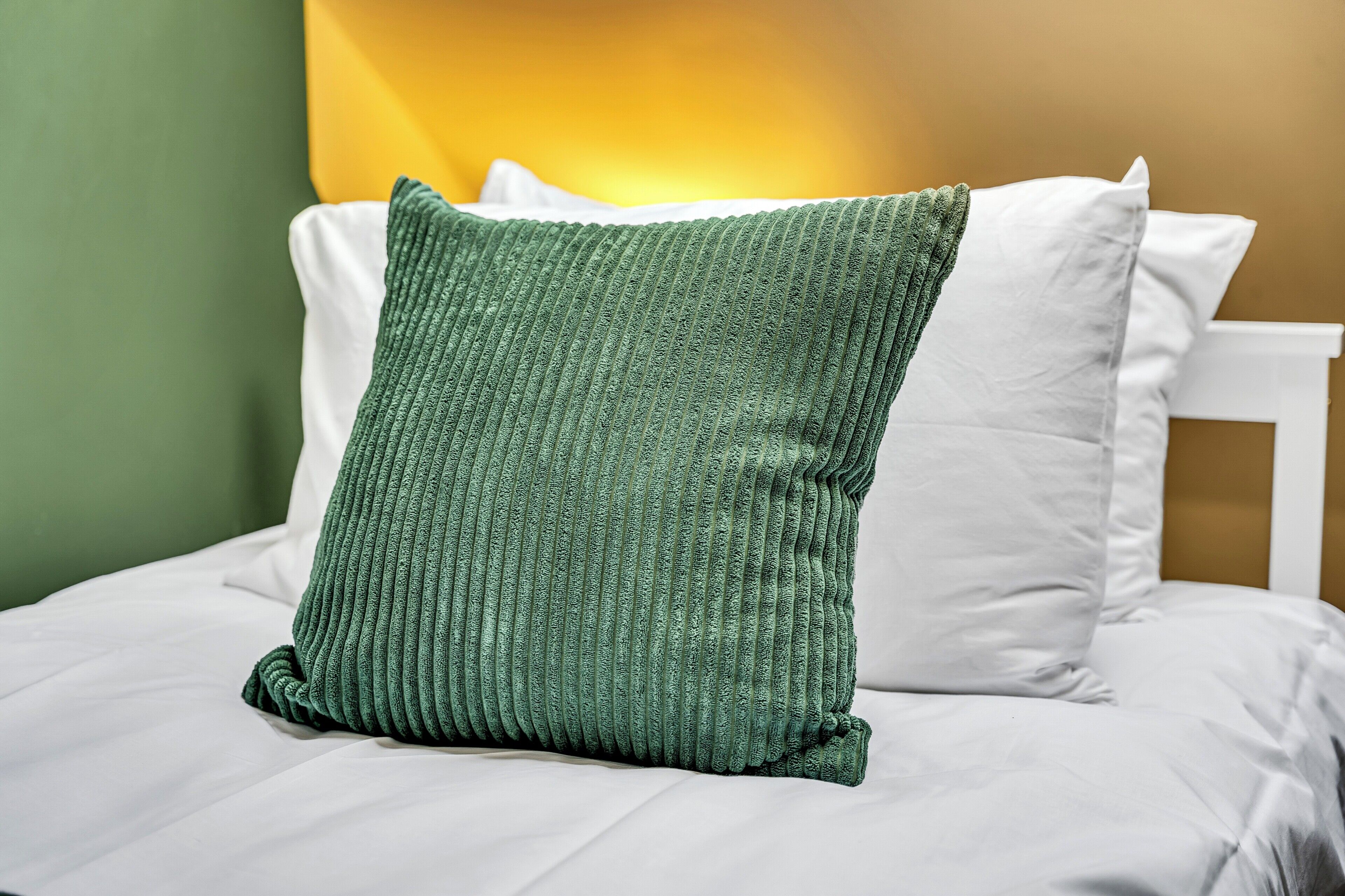 A bed with white bedding and a green textured pillow.