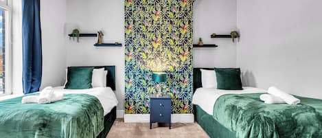 A hotel room with two beds, a nightstand, a wall-mounted shelf, and a window with curtains.