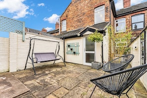 A courtyard with a swing set, a potted plant, and a black chair.