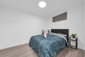 Une chambre à coucher avec un lit, une table de chevet, une plante en pot et une fenêtre avec des stores.