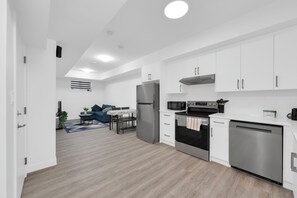 A modern kitchen with stainless steel appliances, white cabinetry, and a dining area with a blue sofa. - 1BHK Close to Downtown/Whyte Ave/UOFA 10947 (Edmonton)