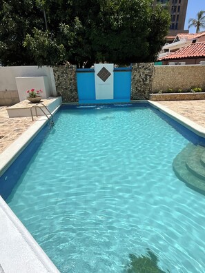 A swimming pool with clear blue water, surrounded by a stone wall and a blue gate. - Beachfront House (Magdalena)