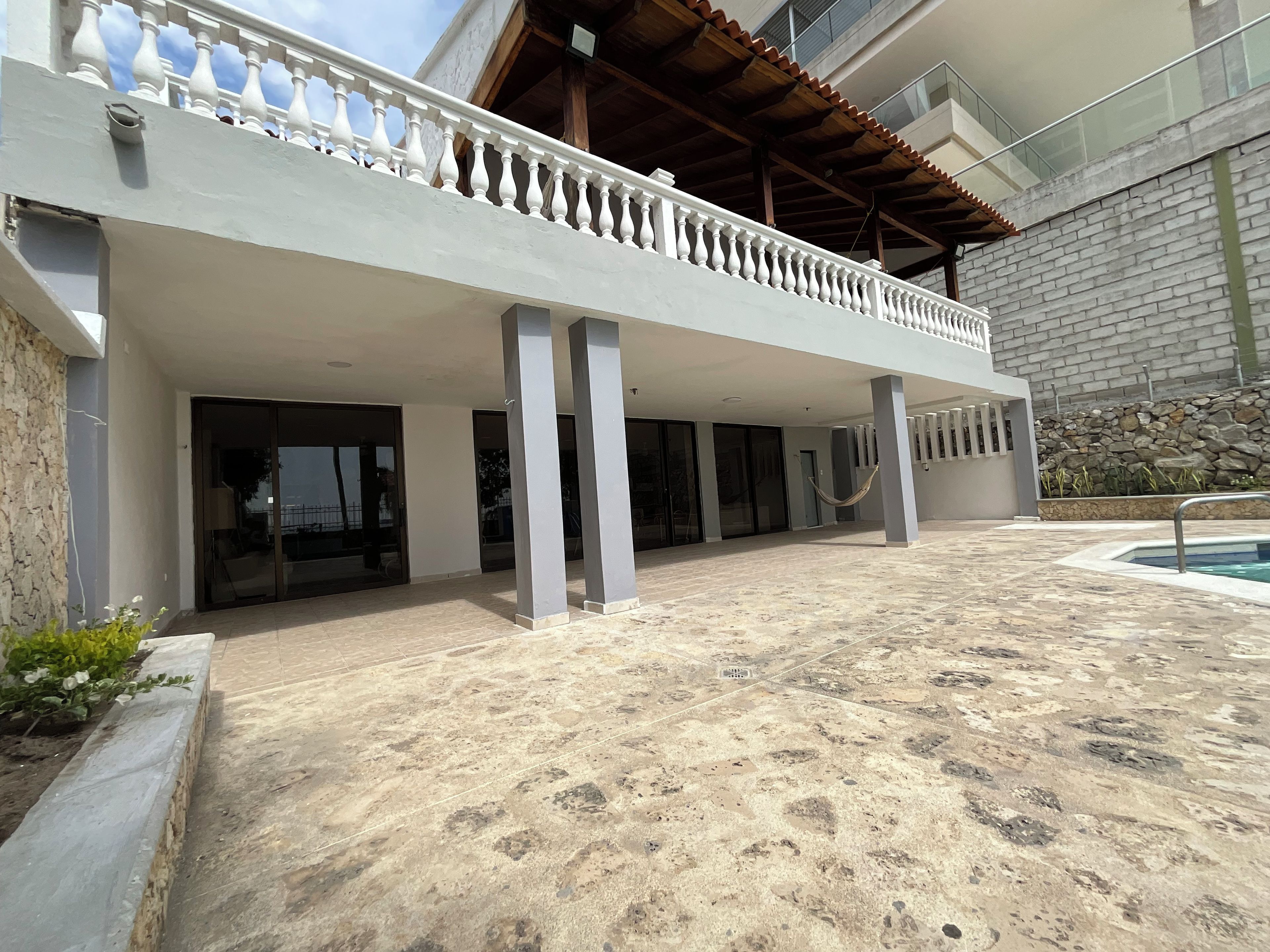 A modern building with a covered outdoor area, a pool, and a stone wall.