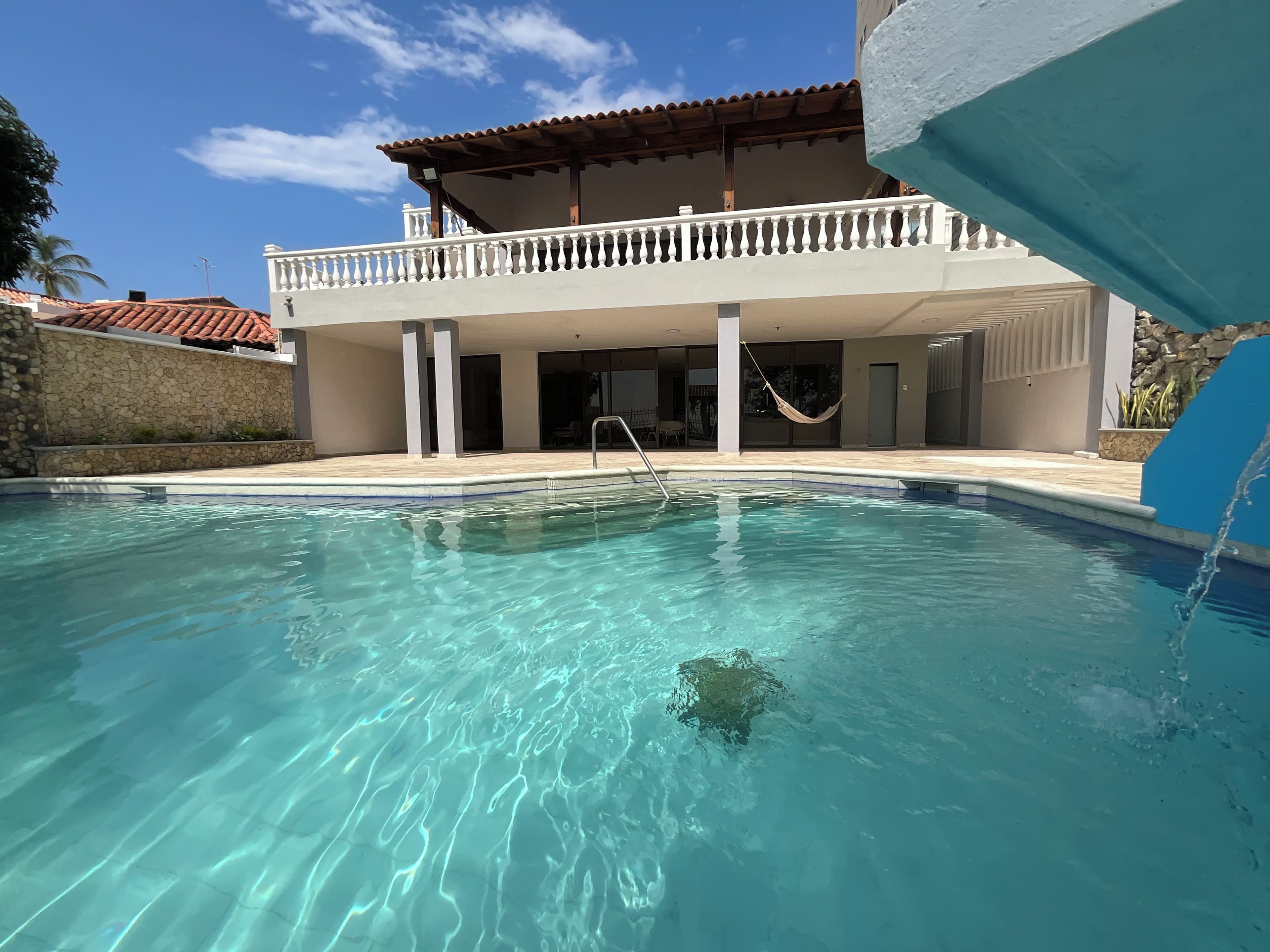 Ein Schwimmbecken mit klarem Wasser, ein weißer Balkon und eine Steinmauer.