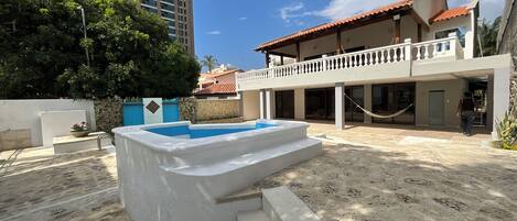 A pool area with steps leading into it, surrounded by a building with a balcony and a tall residential building in the background.