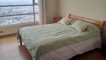 A bedroom with a large window, a bed with a wooden headboard, and a nightstand.