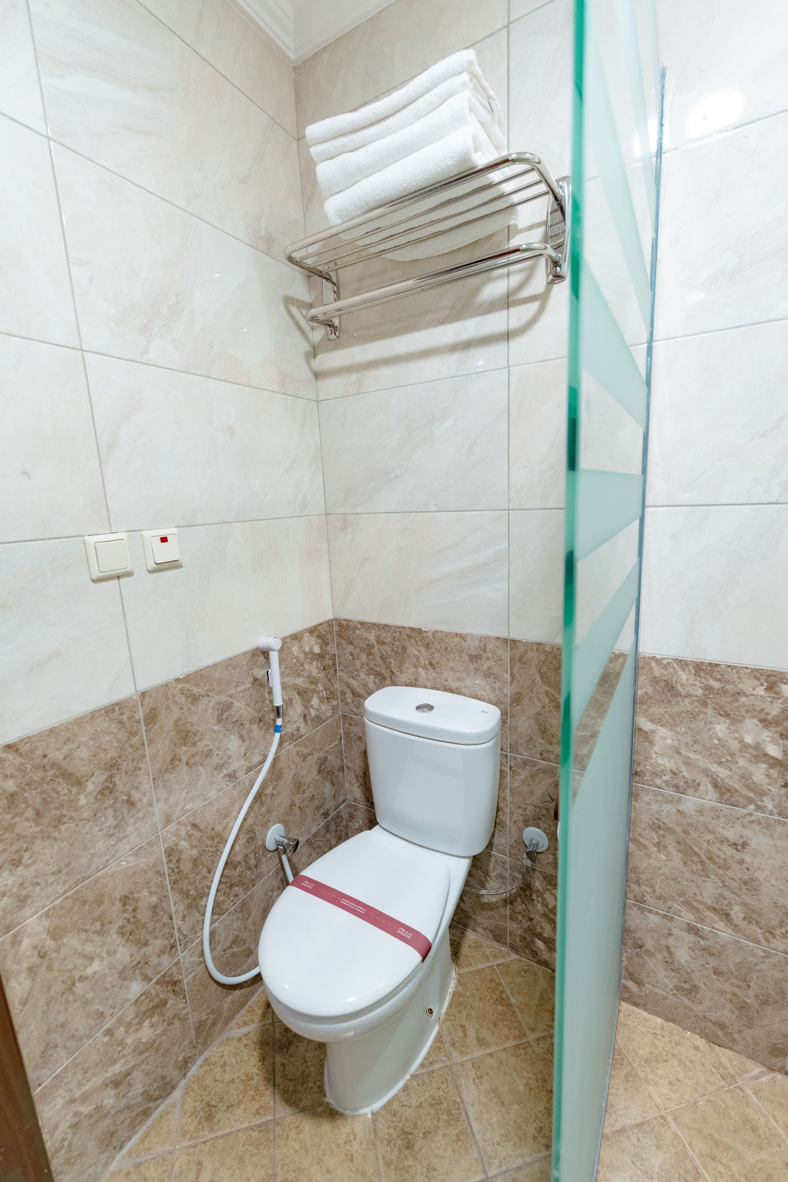 Un baño con inodoro, cabina de ducha de vidrio y toallero con toallas dobladas.