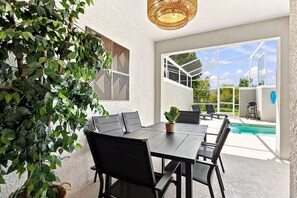 Ein Essbereich im Freien mit Tisch und Stühlen, einer hängenden Lampe und Blick auf einen Swimmingpool.