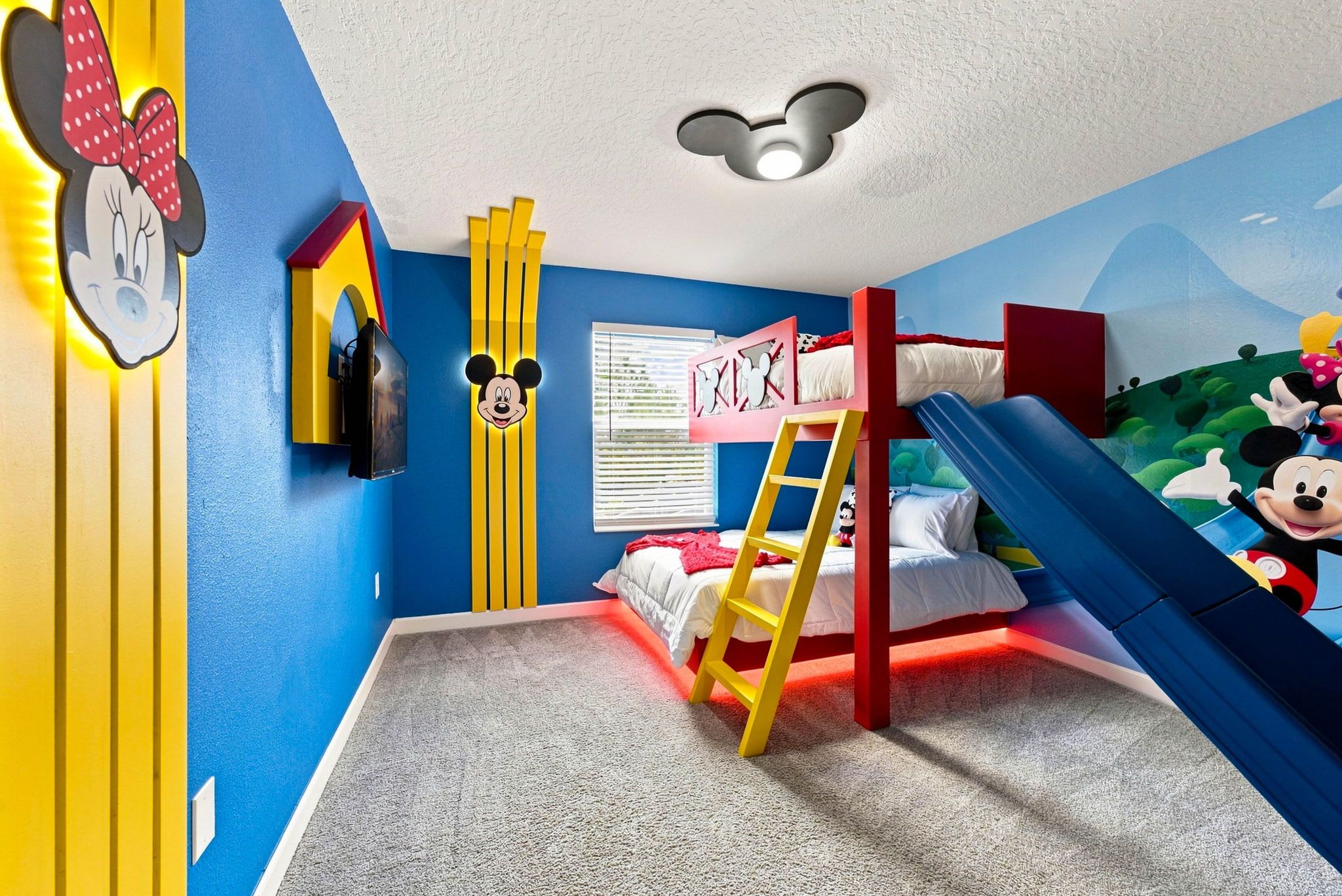 A child's bedroom with a bunk bed, a slide, and Mickey Mouse decorations.