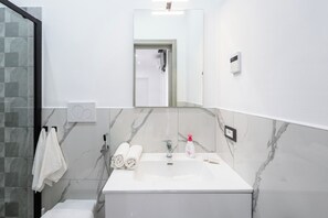 A bathroom with a white sink, a mirror, a shower, and a towel rack. - P&P Apartment (Forio)