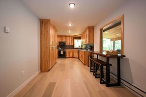 A modern kitchen with wooden cabinets, a central island, and a dining area with benches. - Winter Getaway at Northern Lights Lodge (Spooner)