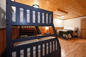 A bunk bed room with wooden walls and ceiling, a wooden door, and a bedside table with a lamp. - Winter Getaway at Northern Lights Lodge (Spooner)