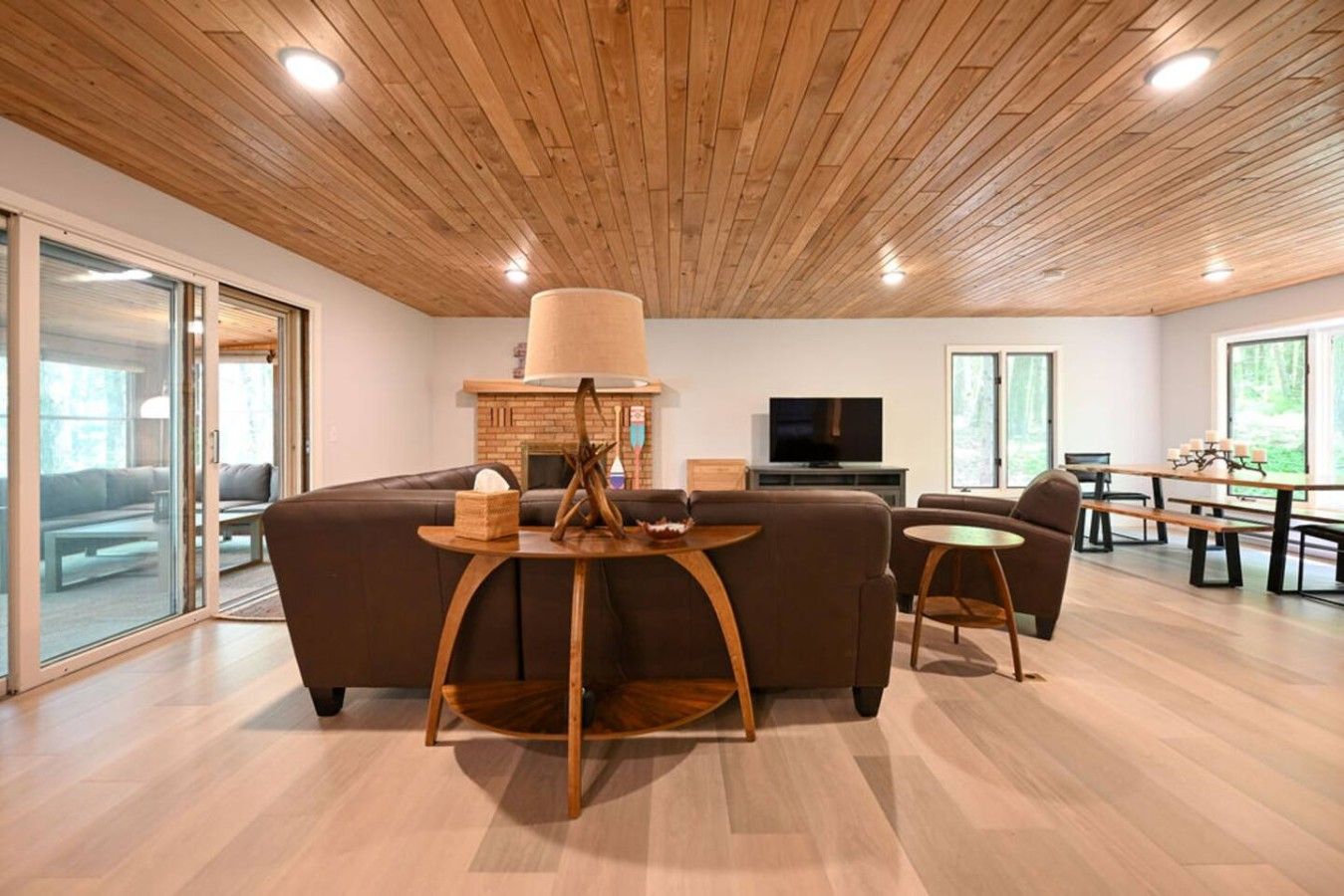 Un salon moderne avec un plafond en bois, une cheminée, un téléviseur et un coin repas comprenant une table et des chaises.