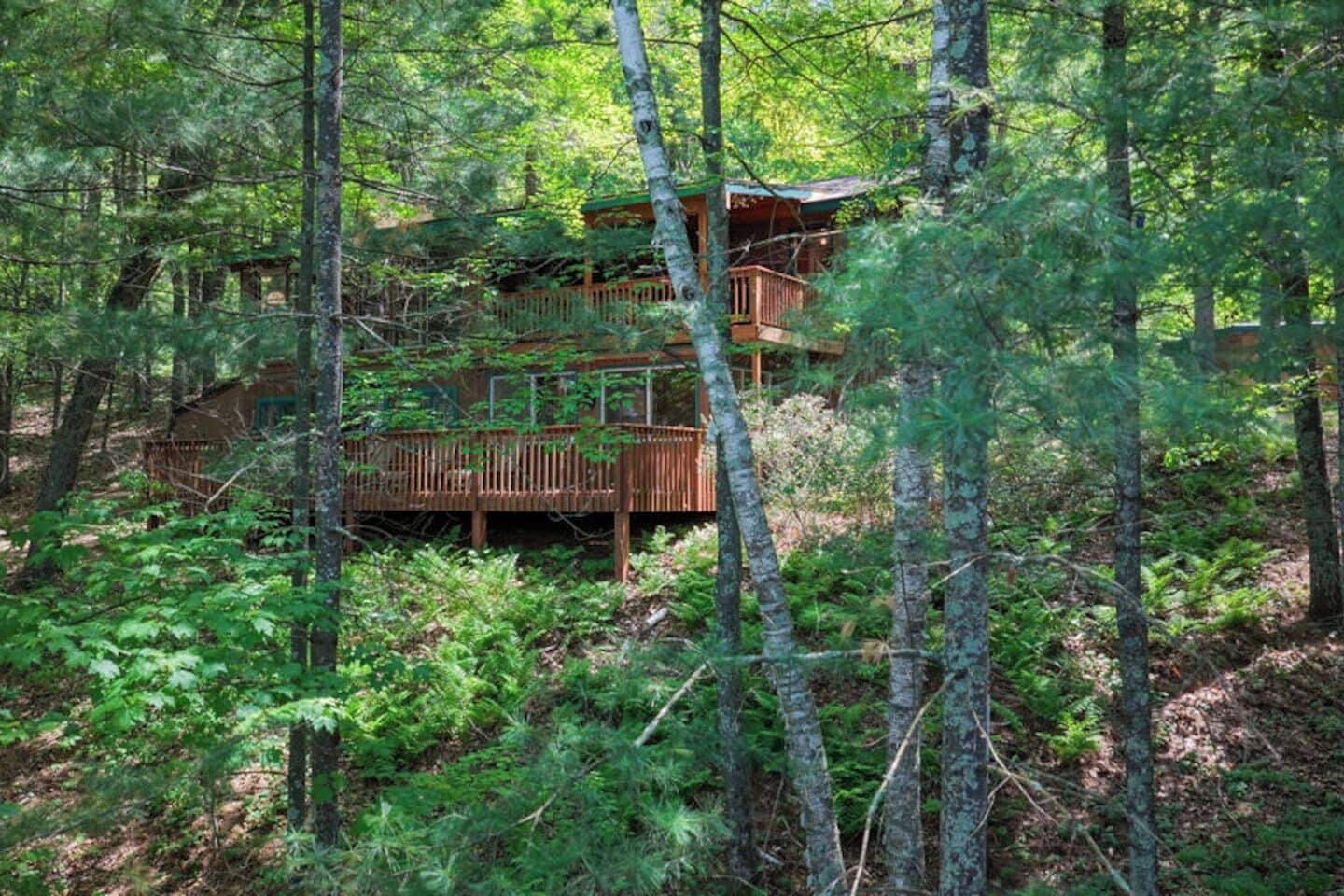 A cabin surrounded by dense forest with a wooden deck and multiple levels.