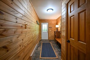 A hallway with wooden walls, a door, a bench, a rug, and a lamp. - Winter Getaway at Northern Lights Lodge (Spooner)