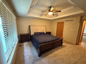 A bedroom with a bed, nightstands, a ceiling fan, and a door.