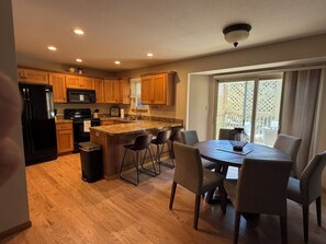 A kitchen with wooden cabinets, a black refrigerator, a microwave, and a dining area with a table and chairs.