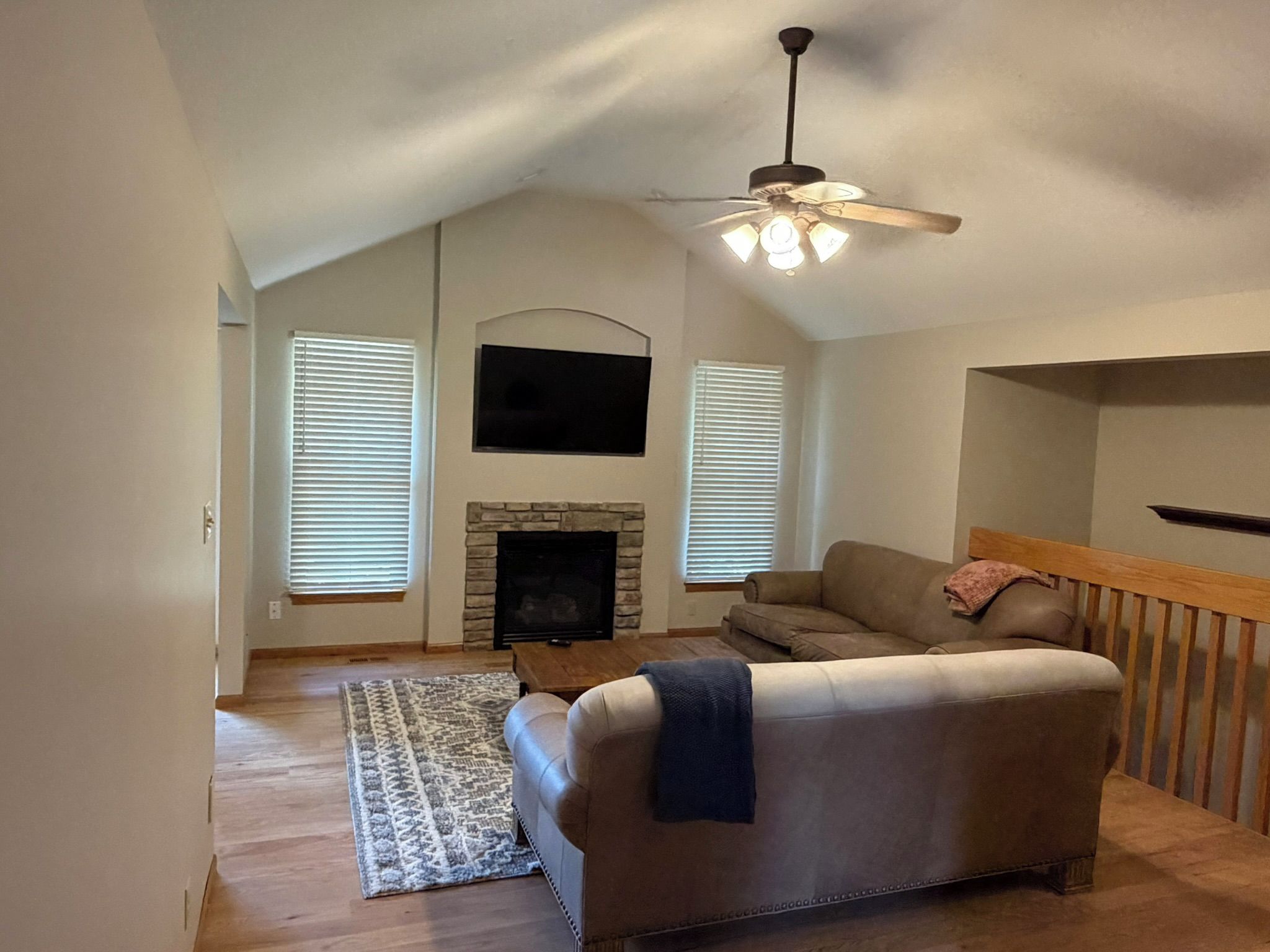 A living room with a stone fireplace, a ceiling fan, a sofa, and a television mounted on the wall.