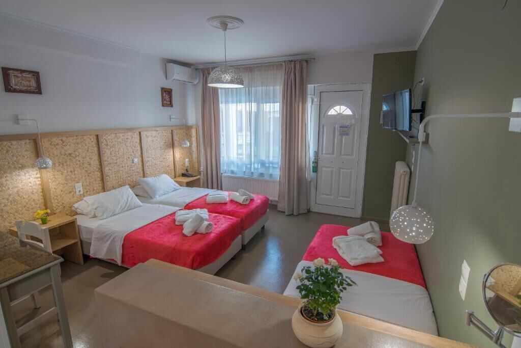 Una camera d'albergo con due letti, una scrivania, una sedia, una televisione e una finestra con tende.