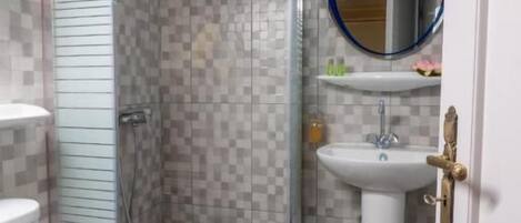 Un baño con cabina de ducha de vidrio, inodoro, lavamanos y espejo.
