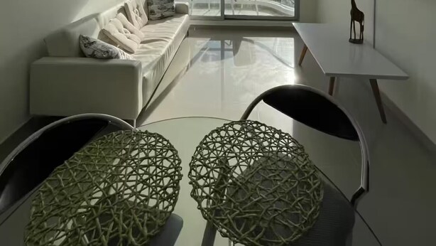Ein modernes Wohnzimmer mit einer Couch, zwei Sesseln, einem kleinen Tisch und einem großen Fenster mit Blick auf das Meer.