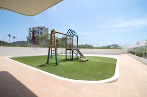 A playground with a swing set and slide, surrounded by a paved area and a grassy patch. - Oceanfront Penthouse Near Rodadero Beach (Gaira)