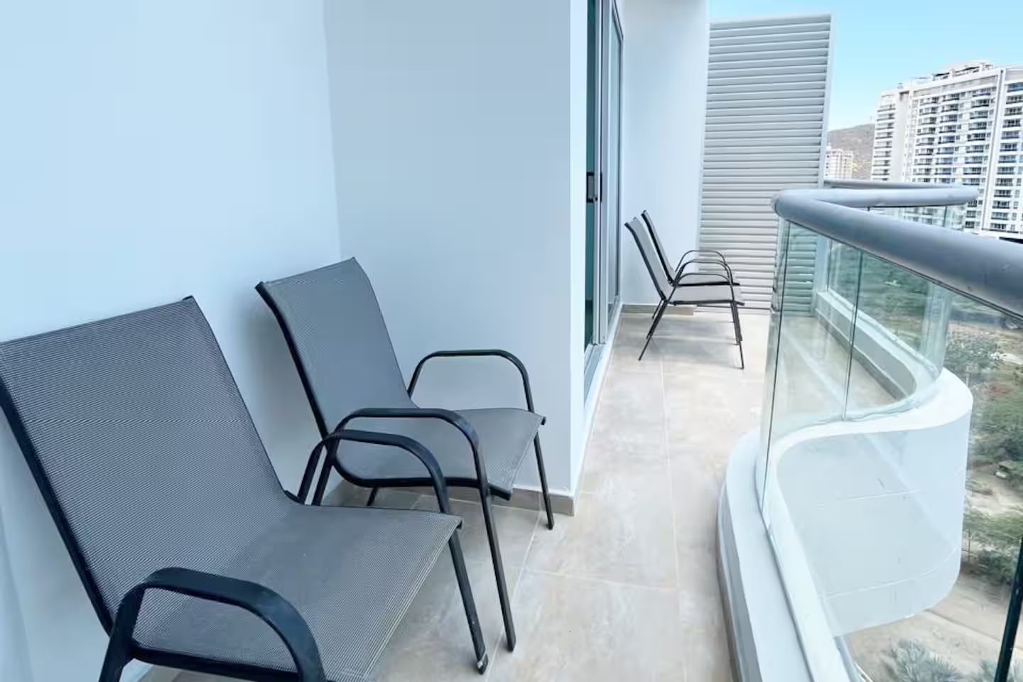 A balcony with two chairs and a glass railing overlooking a cityscape.