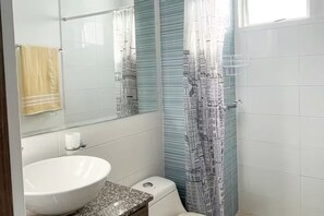 Ett badrum med ett vitt handfat, en toalett och en duschdraperi med ett motiv av en stadsbild.