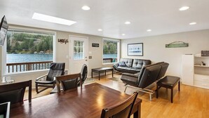 A spacious living area with a wooden dining table, leather sofas, and a view of a lake through large windows. - Secluded 1BR Lakefront - Dock - Deck (Port Angeles)
