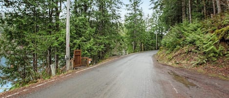 Eine kurvenreiche Straße führt durch ein bewaldetes Gebiet, links ist ein Holzbau zu sehen.