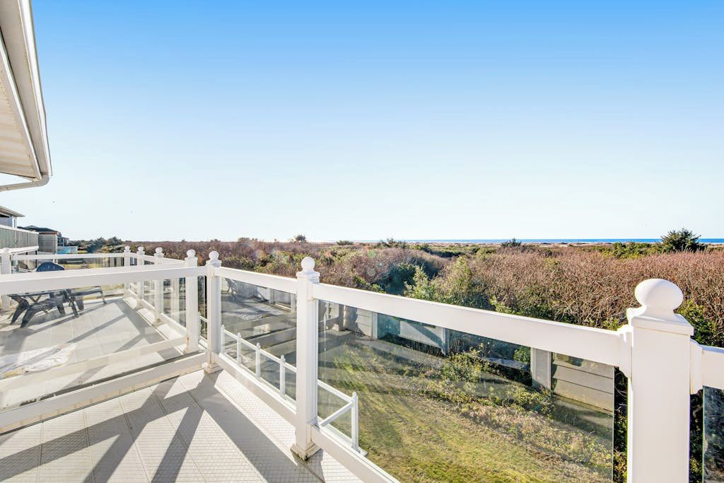 Un balcon doté d’une balustrade blanche, d’où l’on peut admirer un paysage verdoyant et une vue lointaine sur la mer.