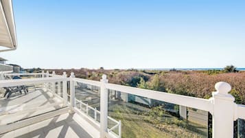 Un balcon doté d’une balustrade blanche, d’où l’on peut admirer un paysage verdoyant et une vue lointaine sur la mer.