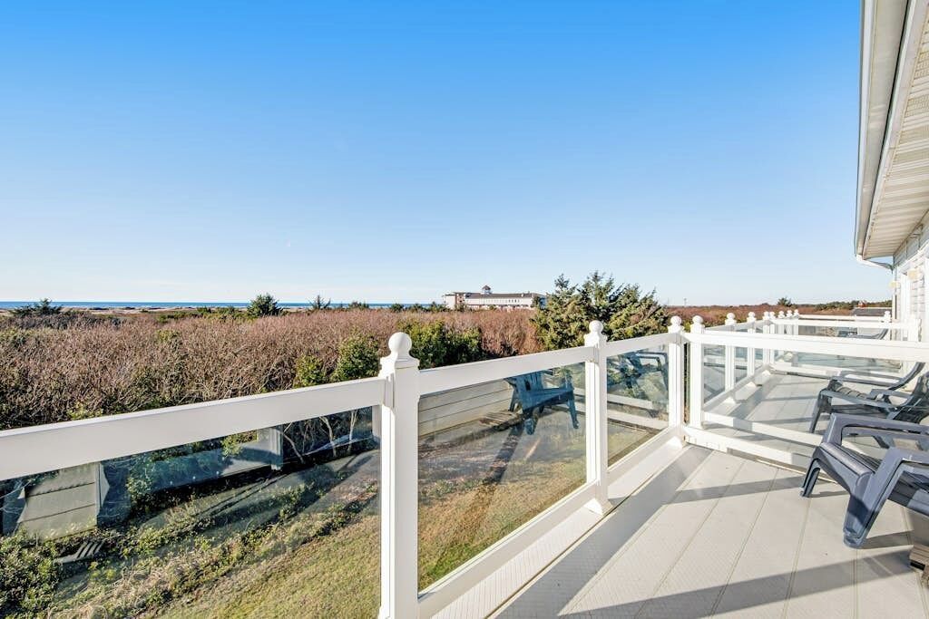 A balcony with a white railing, overlooking a beach and a building in the distance.