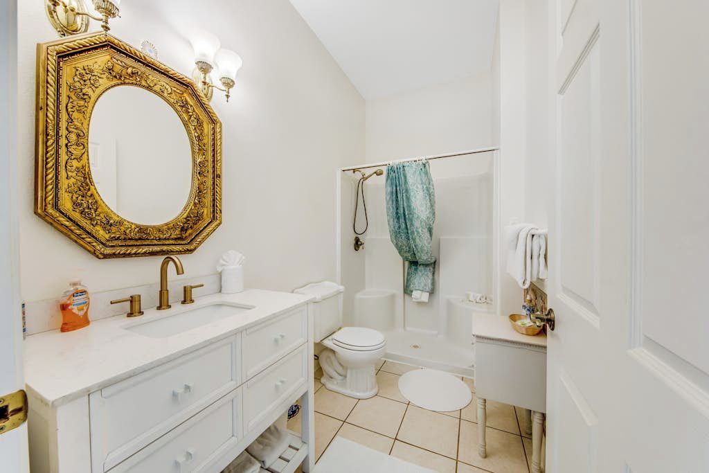 Une salle de bain avec un meuble-lavabo blanc, un miroir à cadre doré, des toilettes blanches, une baignoire et une douche.