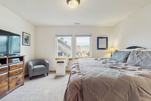 A bedroom with a large bed, a desk with a chair, a heater, and a window with a view of a building. - 2 BR Townhome at the Villages at Roslyn Ridge (Ronald)