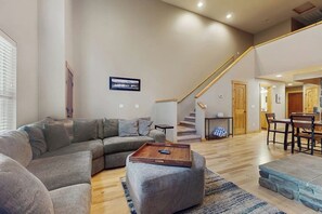 A spacious living area with a sectional sofa, a coffee table, and a staircase leading to an upper level. - 2 BR Townhome at the Villages at Roslyn Ridge (Ronald)