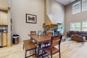 A spacious living area with a dining table, chairs, a sofa, and a kitchen area with a stone backsplash. - 2 BR Townhome at the Villages at Roslyn Ridge (Ronald)