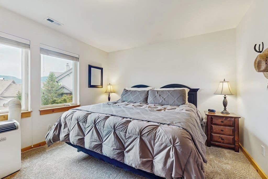 A bedroom with a bed, two bedside lamps, a heater, and a window with blinds.